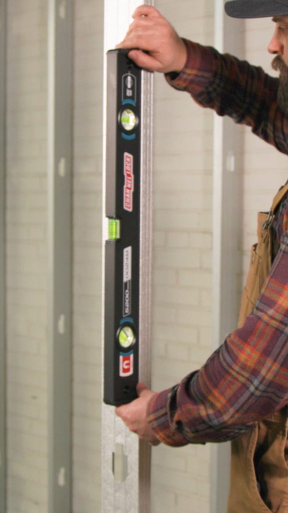 A person in a plaid shirt holds a CHANNELLOCK® level against a doorway frame to check vertical alignment.