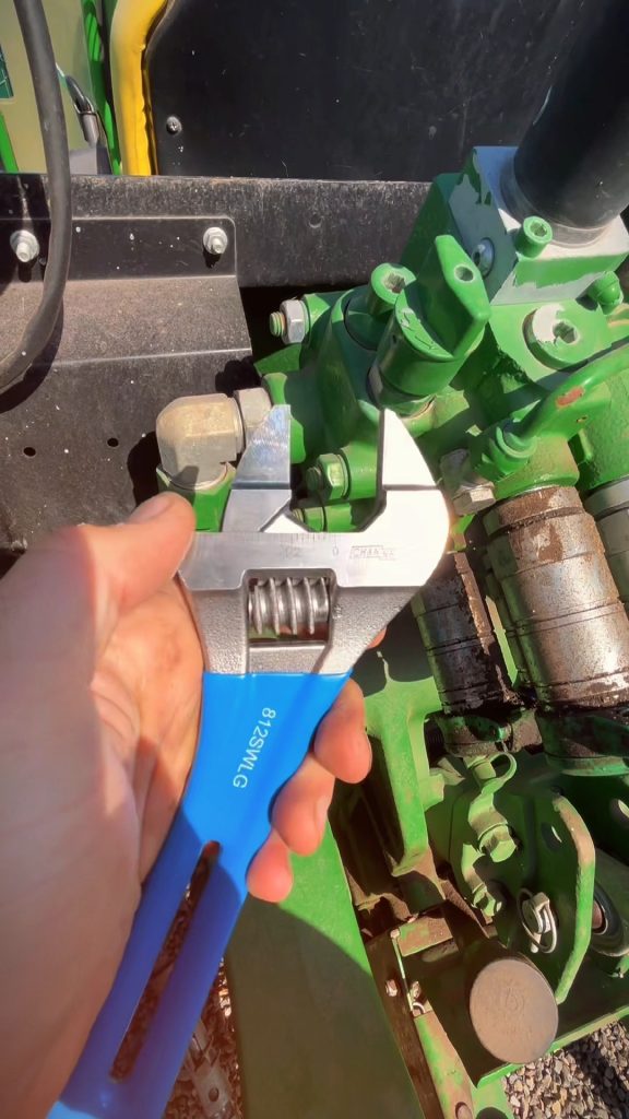 A CHANNELLOCK® adjustable wrench tightens a green valve on green agricultural machinery.