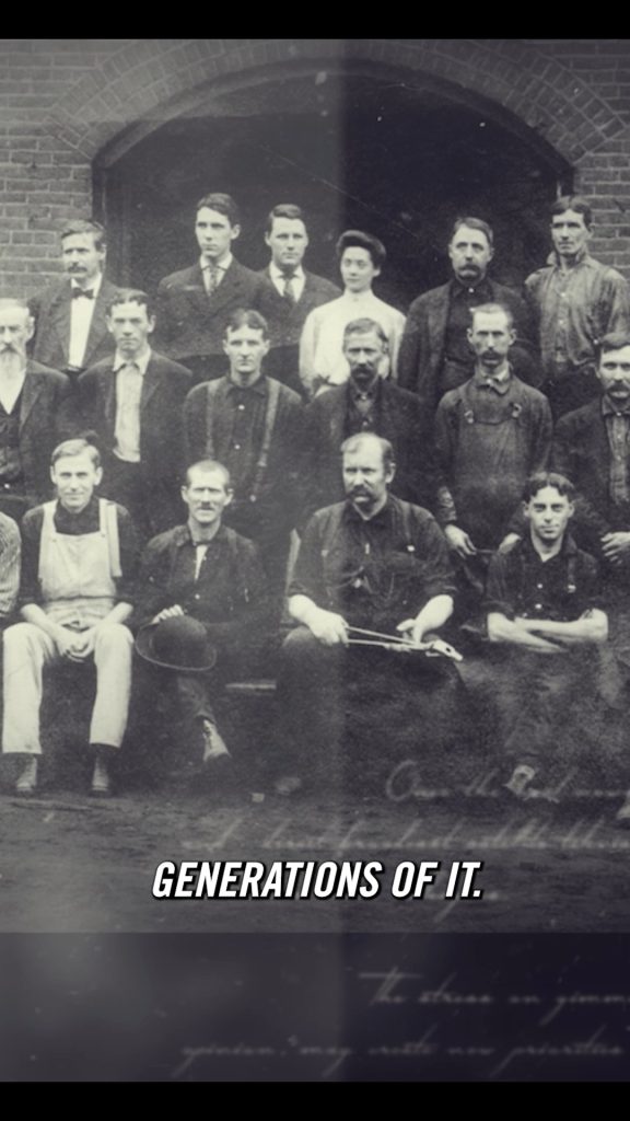 Black-and-white group photograph of men in vintage work attire posing in front of a brick arch, with the caption "GENERATIONS OF IT" across the bottom.