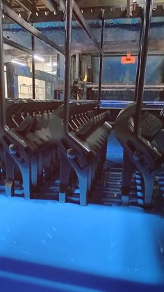 Row of black heavy-duty clamps lined up in a blue tray in an industrial workshop.