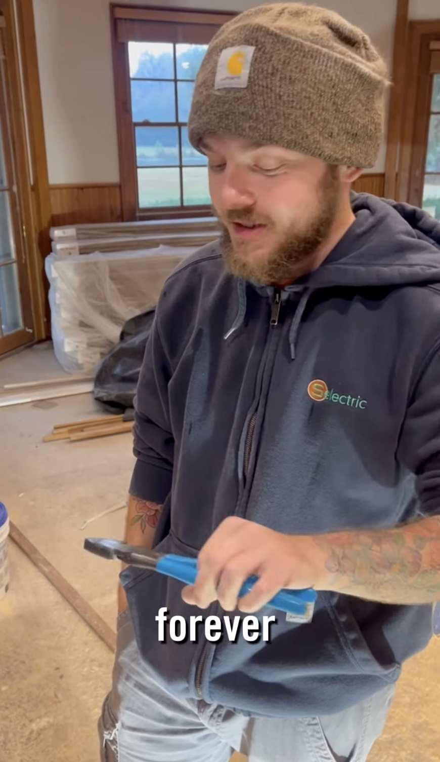 A man in a beanie and hoodie holds CHANNELLOCK® blue-handled pliers in a workshop.
